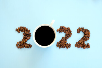 2022 number made of roast coffee beans and cup of coffee on pastel blue background. Happy New Year and Merry Christmas.