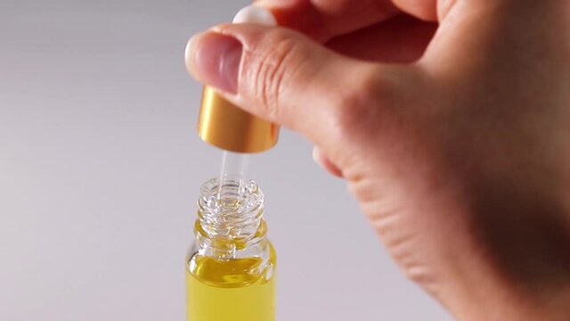 A female hand draws oil into a pipette and drips into a bottle
