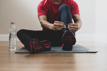 A young athlete wearing red workout clothes is sitting on yoga mat with clean drinking water...