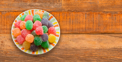 Colorful gummy candies on plate on rustic wooden background.