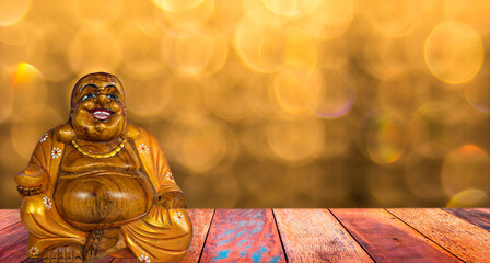 Wooden smiling buddha and gold background with bokeh.