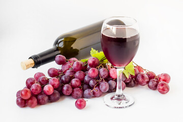 A glass of red wine with wine bottle and red grapes on white surface