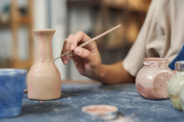 Close-up of unrecognizable potter using paintbrush while applying pink paint on clay vase in...