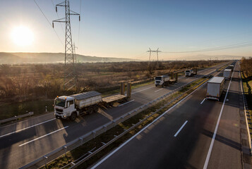 Fleet or Convoy of big transportation trucks in line on a countryside highway under a blue sky