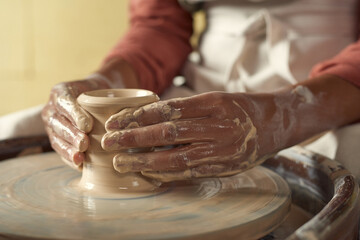 Close-up of unrecognizable black girl with wet dirty hands shaping clay vase on pottery wheel
