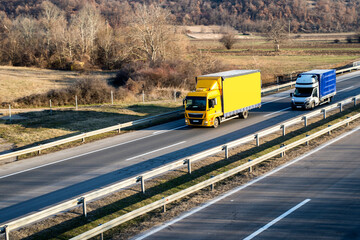 Yellow truck driving on asphalt road in a rural landscape.