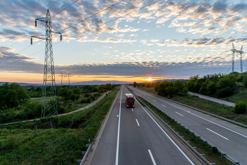 Red truck in the countryside passing through green-blue nature on the highway.