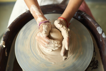 Above view of unrecognizable woman with dirty hands shaping clay while working on pottery wheel