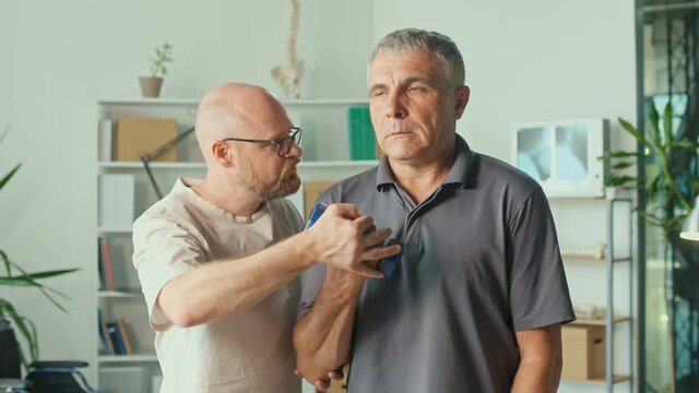 Senior Man a Brain Stroke Doing Dumbbell Exercises as Part of a Rehabilitation Program with a Physiotherapist in a Modern Clinic. Paralysis of the Facial Nerve, Limited Movement. Rehabilitation.
