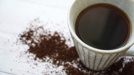 木製の床に散らばるグラインドされたコーヒー豆とコーヒカップ