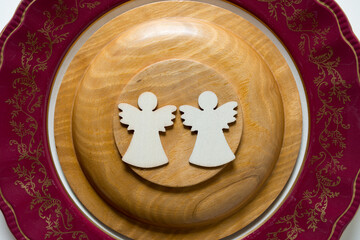 two christmas angel shapes on the bottom of a wooden plate (resting on top of an antique dish)