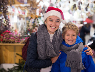 Portrait of cute preteen boy having fun at Christmas street market with mother. Happy family moments