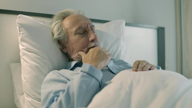 Old man coughing, lying in bed, shortness of breath, symptom of bronchitis