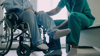 Male caregiver helping mature patient to recover injured leg, physiotherapy