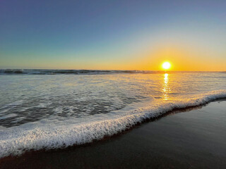 Low angle shot of a wave gently washing over the sandy beach at Chrystal Cove State Park in Orange County California at sunset