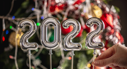 Woman hand is setting the last symbol 2 in the number 2022 on the background of a beautiful...