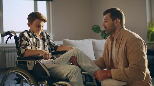 Young man helping injured son, sitting in wheelchair, medical rehabilitation