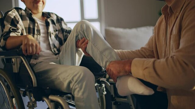 Caring father helping son in wheelchair to do rehabilitation exercises at home