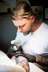A tattoo artist works on a tattoo on the arm of a customer.