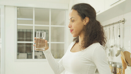 Portrait of happy latin woman drinking a glass of water in kitchen at home. People lifestyle....