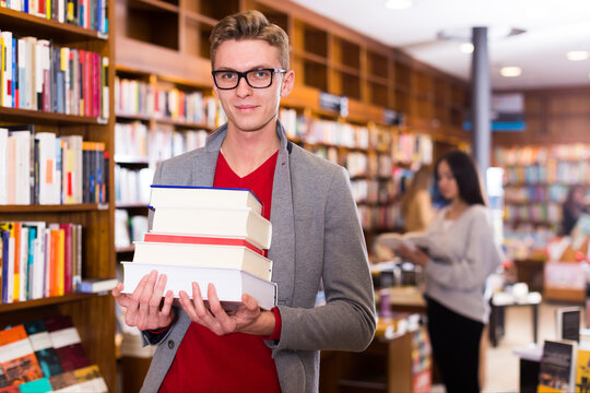 Portrait of young man with stack of books in hands in bookshop