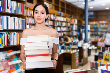 Smiling positive glad attractive girl holding pile of books bought in bookstore