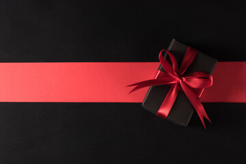 Black Friday sale shopping and Boxing Day concept, Gift box wrapped black paper and red bow ribbon present, studio shot isolated on red and dark background