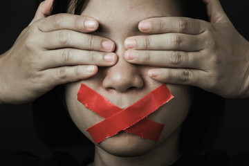 Asian woman blindfold wrapping mouth with red adhesive tape on black background. Freedom speech...