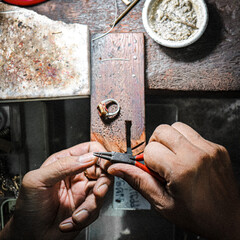 Hands of jewelry maker working on gold setting on wood table