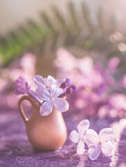 closeup of a purple lilac in a brown clay vase. close-up of lilac petals on a purple floral background. tiny cute bouquet of lilacs standing on the cover of a book