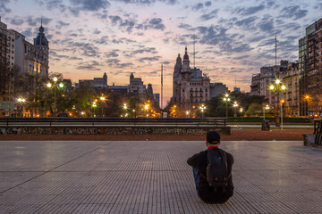 A man staring at a beautiful and colorful sunrise in Congressional Plaza, Buenos Aires, Argentina....