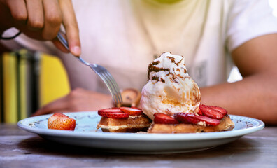 A plate of waffles with fruit. Man's hands preparing to eat it with knife and fork.