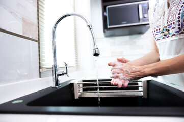Woman washing her hands with soap over sink in luxury kitchen , concept of health