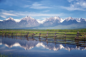 The mountains of the Eastern Sayan Mountains are reflected in the water. Landscape with a wooden fence. Buryatia, Russia