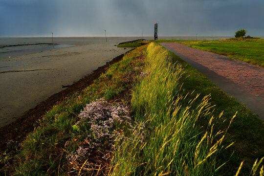 the North Sea coast at the port entrance of Fedderwardersiel (Butjadingen, Germany) with the small lighthouse in sunlight after a heavy rain with dark grey sky