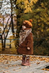 A dreamy little girl in a brown beret and autumn clothes on an autumn background. A smiling child is playing in the autumn park.