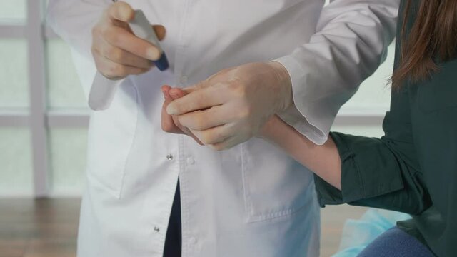 The Doctor Does a Blood Sugar Test and Checks The Blood Sugar Level of A Diabetic Patient with a Lancet Glucometer at the Tip of His Finger. Analyzes and Consultations in the Clinic. Close-up.