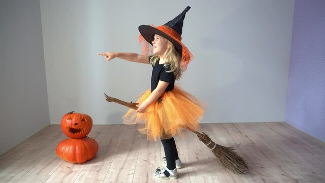 Halloween. A child dressed as a witch sits on a broomstick and points forward.