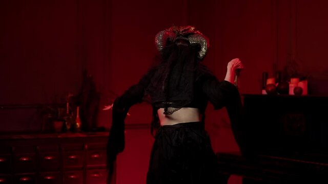 voodoo woman with ram horns, day of the Dead make-up praying over bonfire with eagle claws with her back to the camera, turns sharply and glanced. halloween calavera skull with flowers, sewn mouth