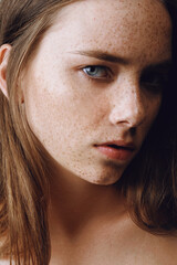 Portrait of a beautiful girl with long hair, perfect skin and freckles looking in camera