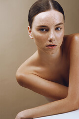 portrait of a beautiful woman with perfect freckled skin and nude makeup looking into camera