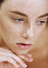 Young beautiful girl with freckles, perfect skin and nude makeup touched her face