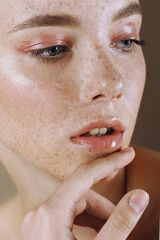 Young beautiful girl with freckles, perfect skin and nude makeup touched her face