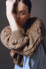 Young beautiful girl with freckles face in cozy knitted autumn sweater rests on her arm