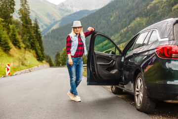 Woman with car near countryside road through mountain Alps