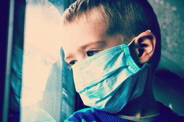 Young ill boy at the hospital looks at window and wants to go home. Kid using the medical face mask . Protection against corona virus. Sick child breathes through a protective mask
