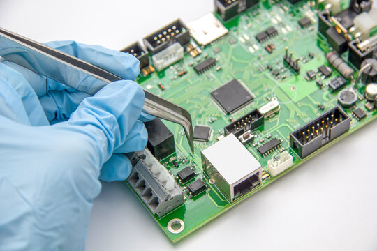 Hand in blue glove holds tweezers with smd compenent chip for pcb