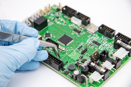 Hand in blue glove holds tweezers with smd compenent chip for pcb