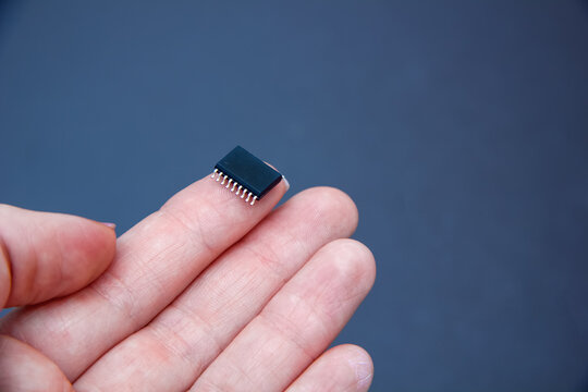 Hand holds chip compenent. Embedding the chip under human skin, microcontroller implanting NFC technology