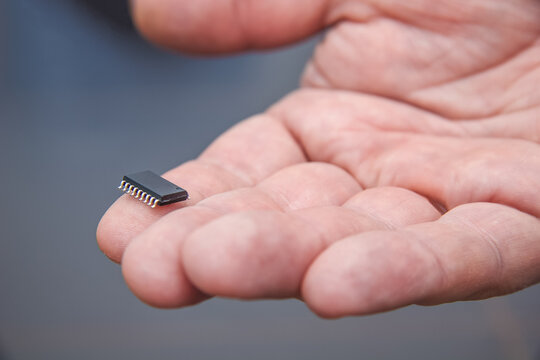 Hand holds chip compenent. Embedding the chip under human skin, microcontroller implanting NFC technology